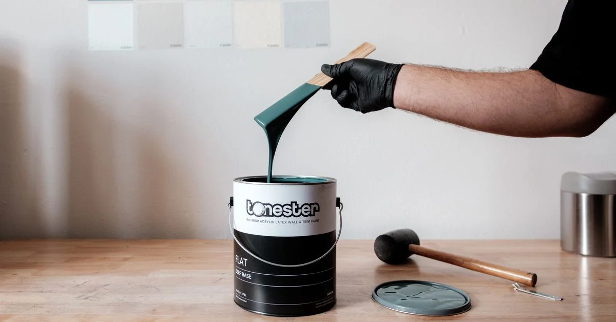 Bras tenant un pinceau au-dessus d'un seau de peinture verte, outils sur une table en bois.