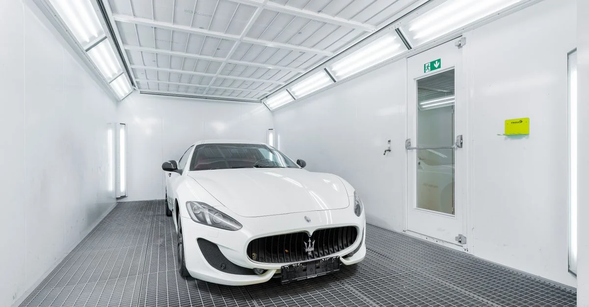 Voiture de luxe blanche à l'intérieur d'une cabine de peinture bien éclairée, présentant un design élégant et sophistiqué.
