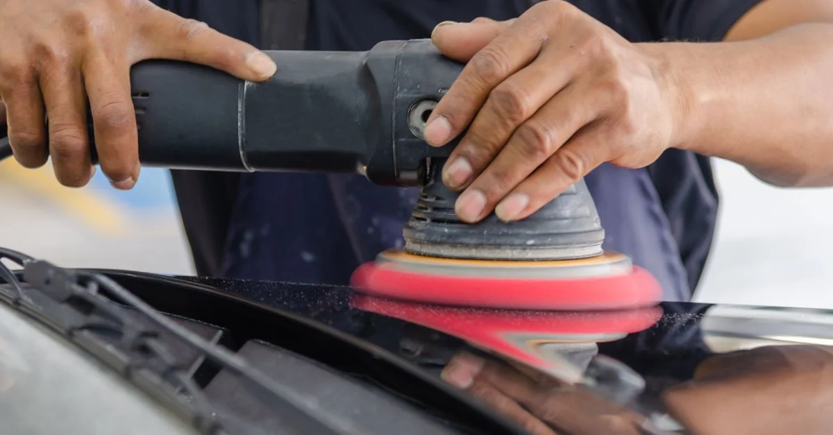 Gros plan sur un mécanicien polissant une voiture avec un outil de polissage électrique.