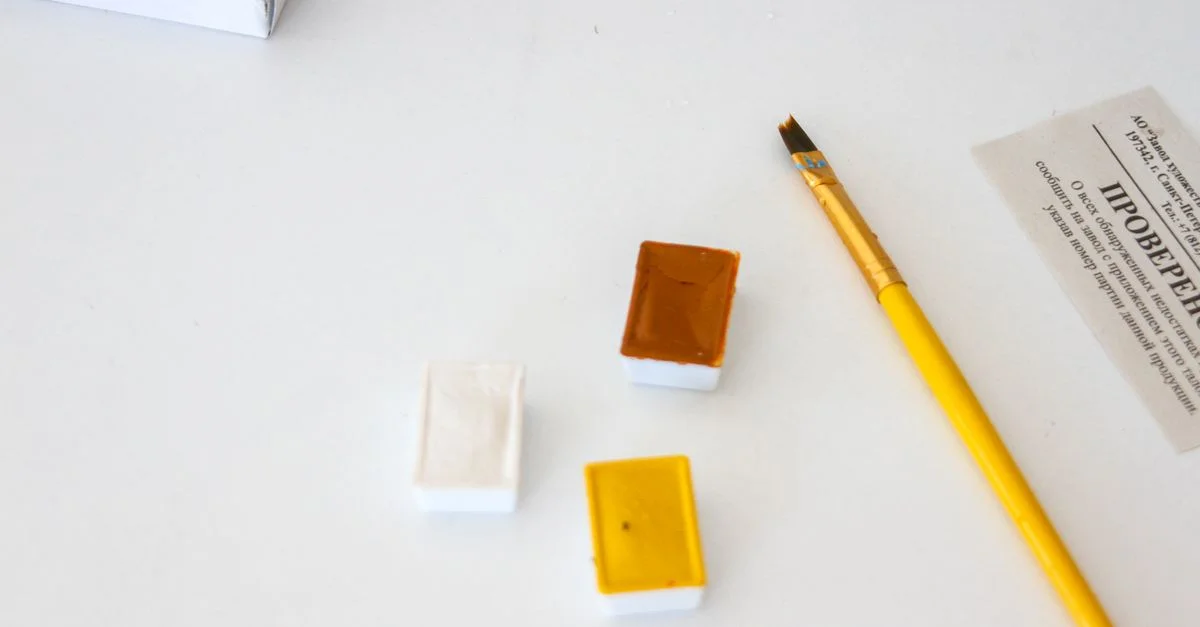 Un gros plan de godets d'aquarelle et d'un pinceau sur une table blanche, idéal pour les artistes.